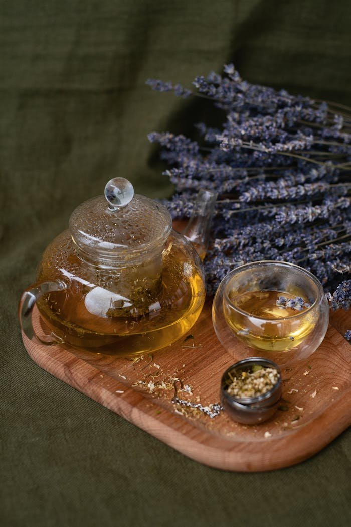 Glass teapot with lavender herbal tea on wooden tray. Perfect for calming moments.