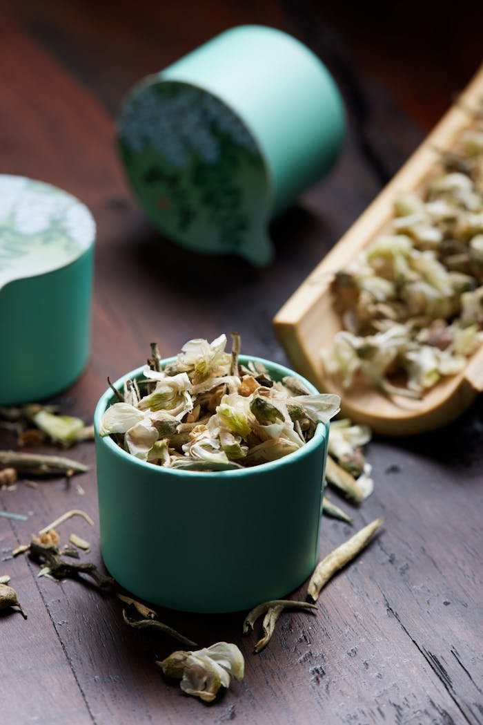Close-up of dried herbs and leaves in a green cup on a wooden surface.